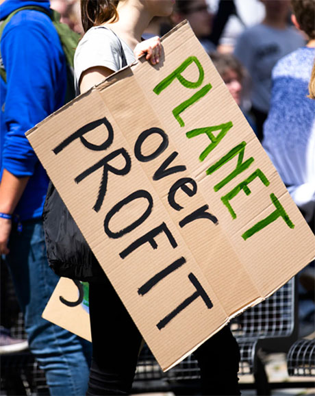 A woman from a social impact agency holding a sign reading "planet over profit".